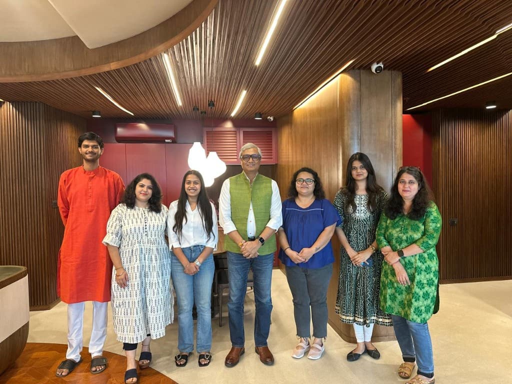 Team members in business and traditional dress in a warm wood-paneled office space.